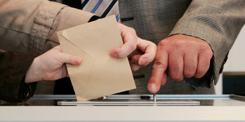 Pray for elections - a person posting in their vote to a ballot box.